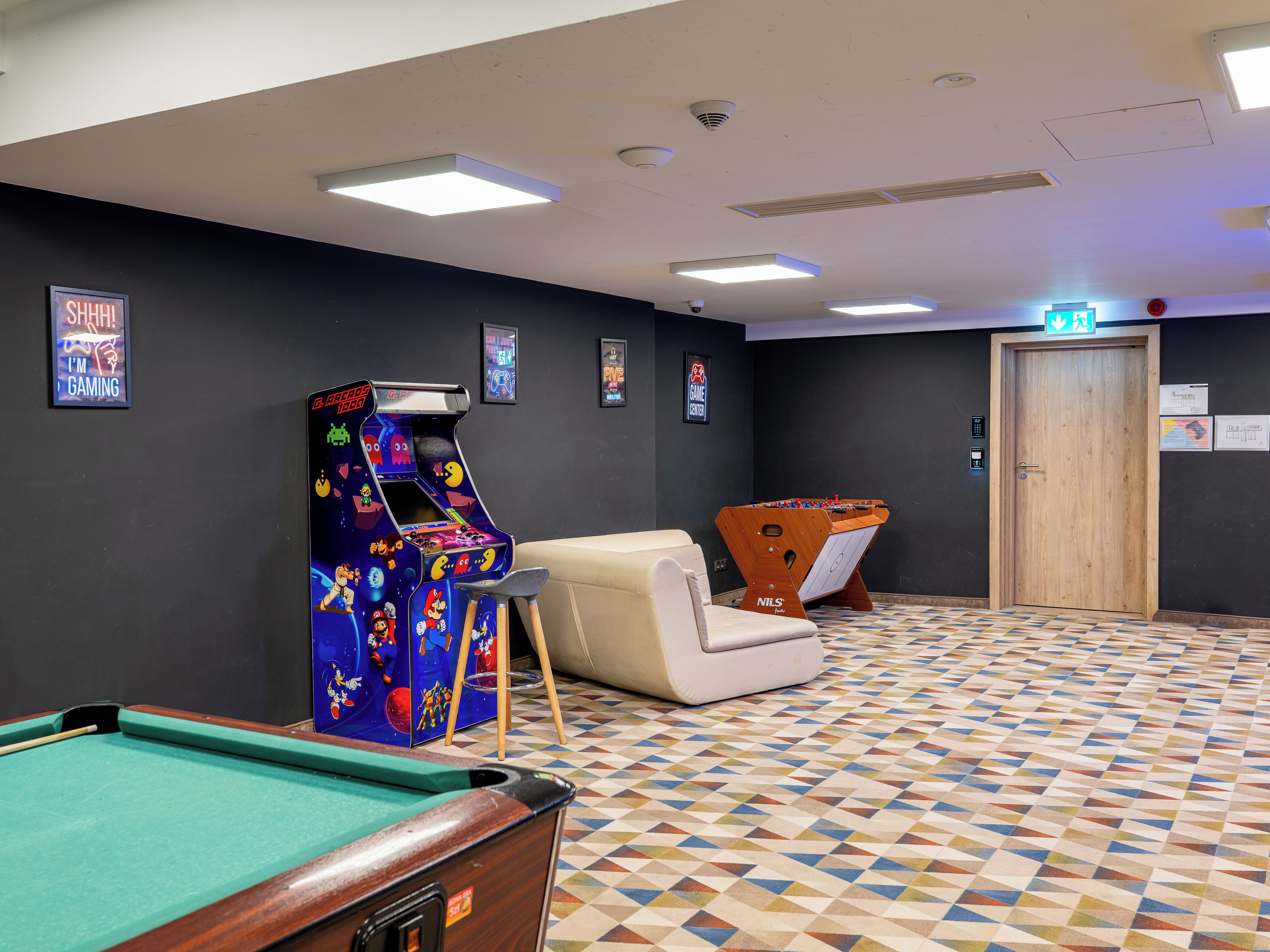 Une salle avec une table de billard, un baby-foot et des jeux d’arcade.