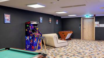 A room with a pool table, a foosball table, and arcade games.