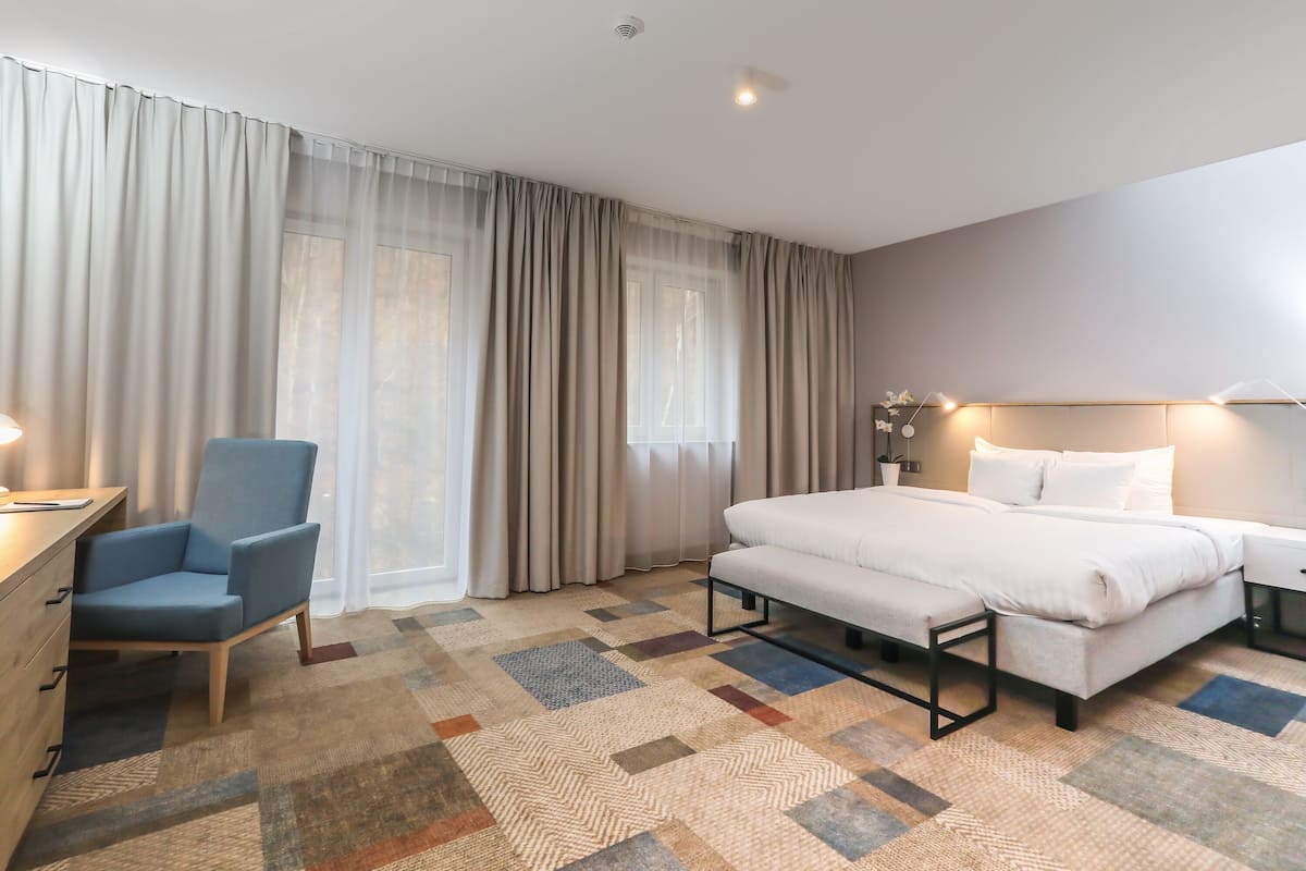 A hotel room with a bed, a desk, a chair, and a large window with curtains.