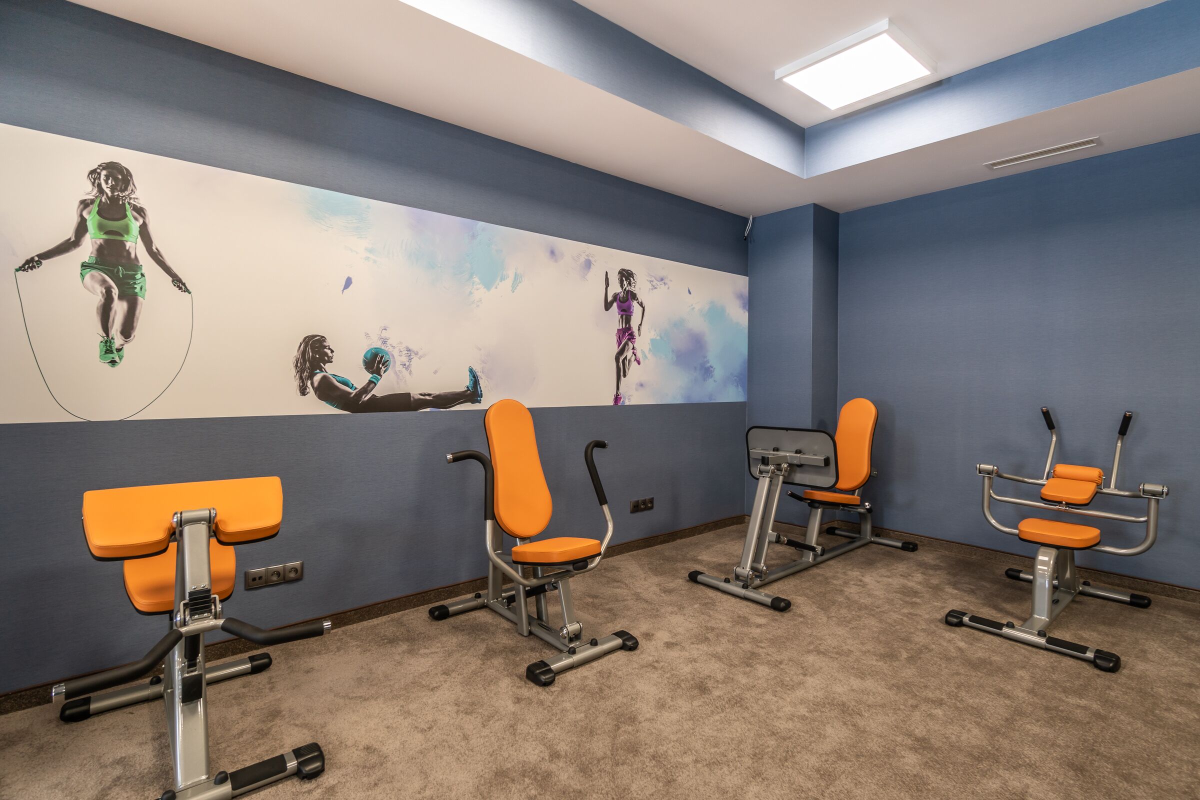 Una habitación con equipo de ejercicio, una pared azul y un mural de atletas.