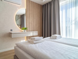 A hotel room with a wooden wall, a mirror, a plant, a bedside table, and a bed with towels.