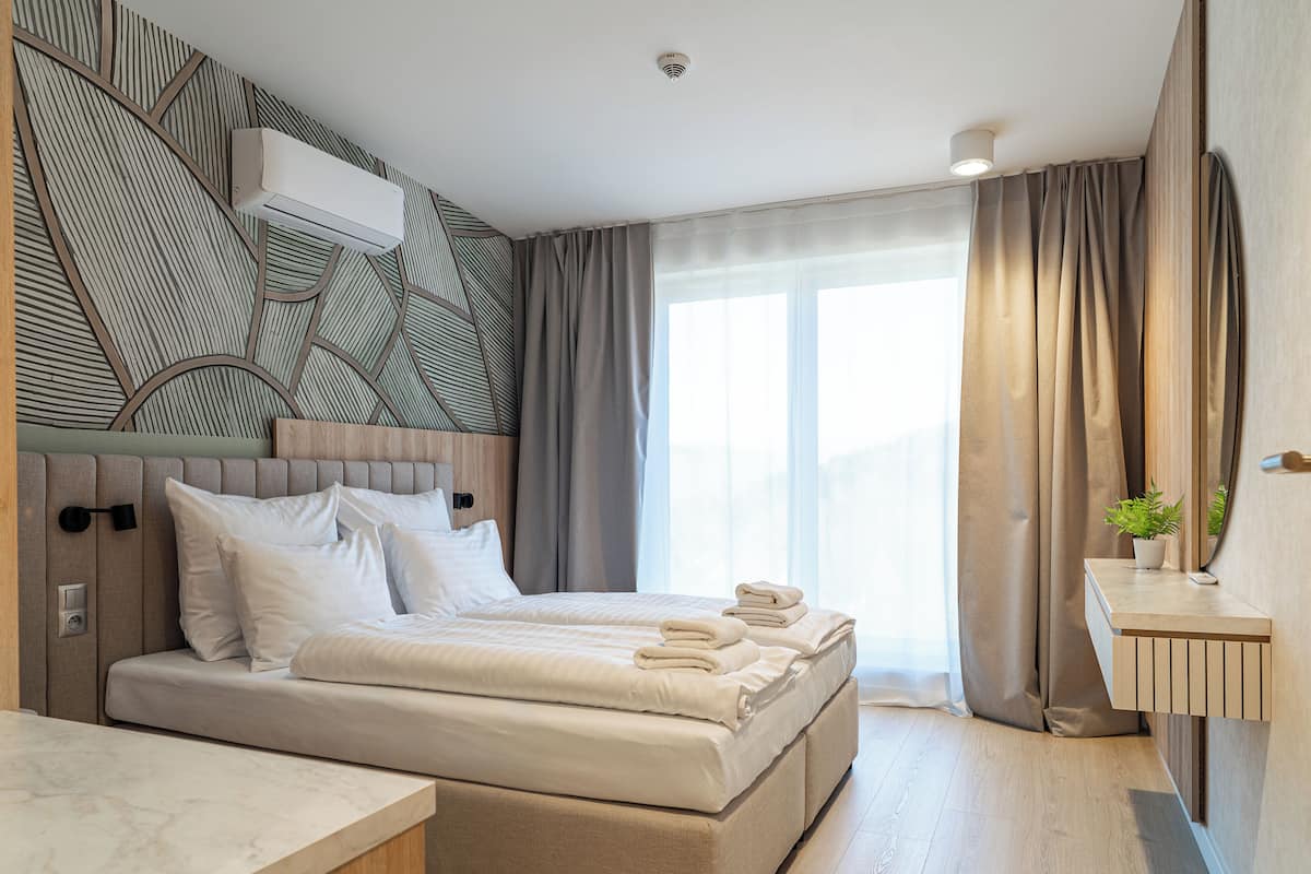 A modern hotel room with a large bed, a bedside table, a mirror, and a window with curtains.
