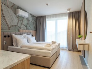 Moderni hotellihuone, jossa on suuri sänky, yöpöytä, peili ja ikkuna, jossa on verhot.