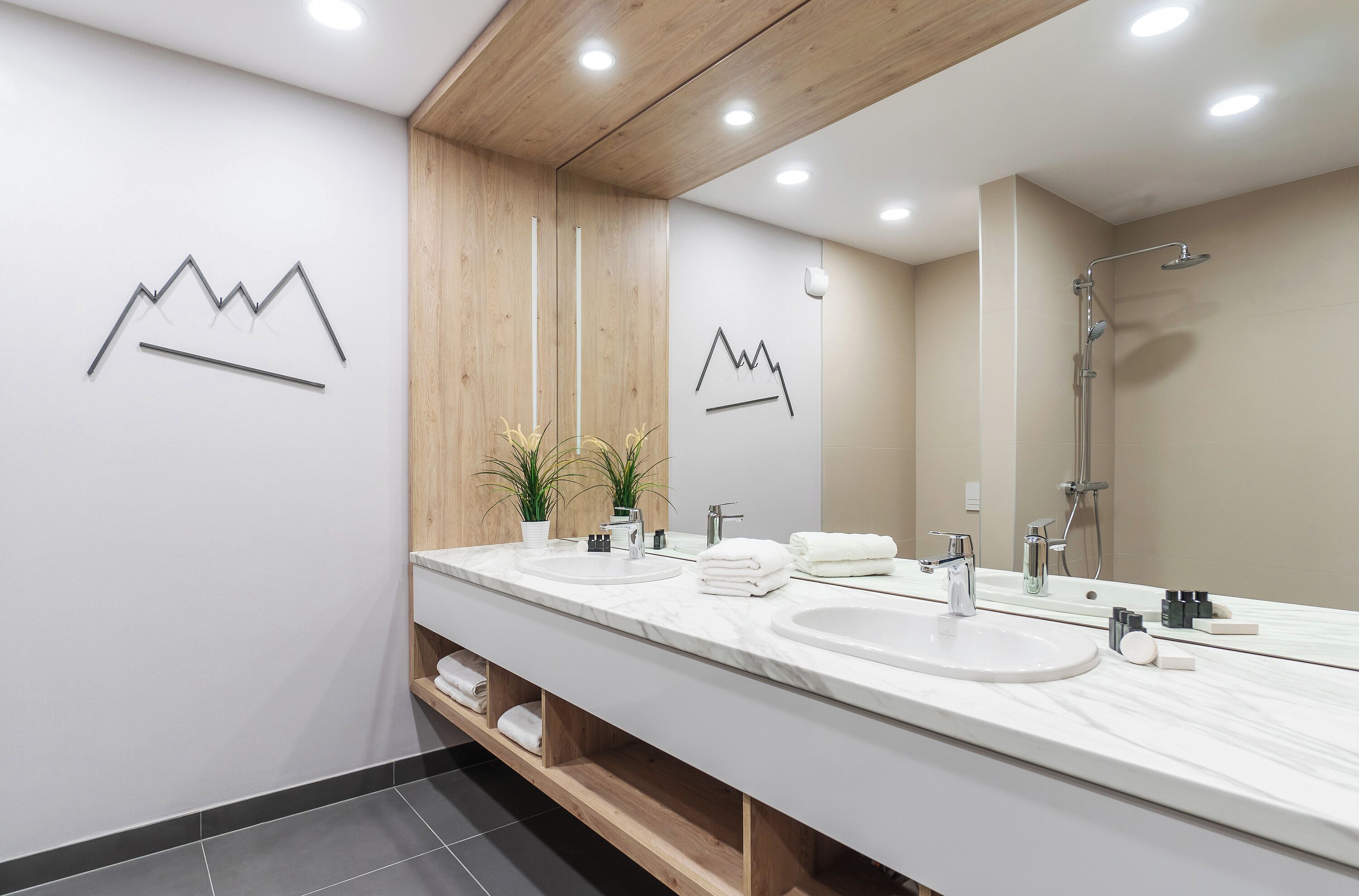 A modern bathroom with two sinks, a shower, wooden paneling, and minimalist decor.