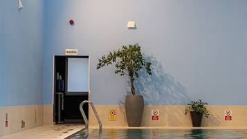 An indoor swimming pool with a sauna sign, a plant, and a no diving sign.