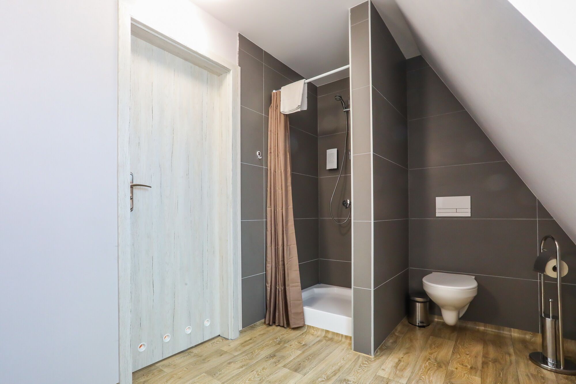 A modern bathroom with a shower, toilet, and a door leading to another room.