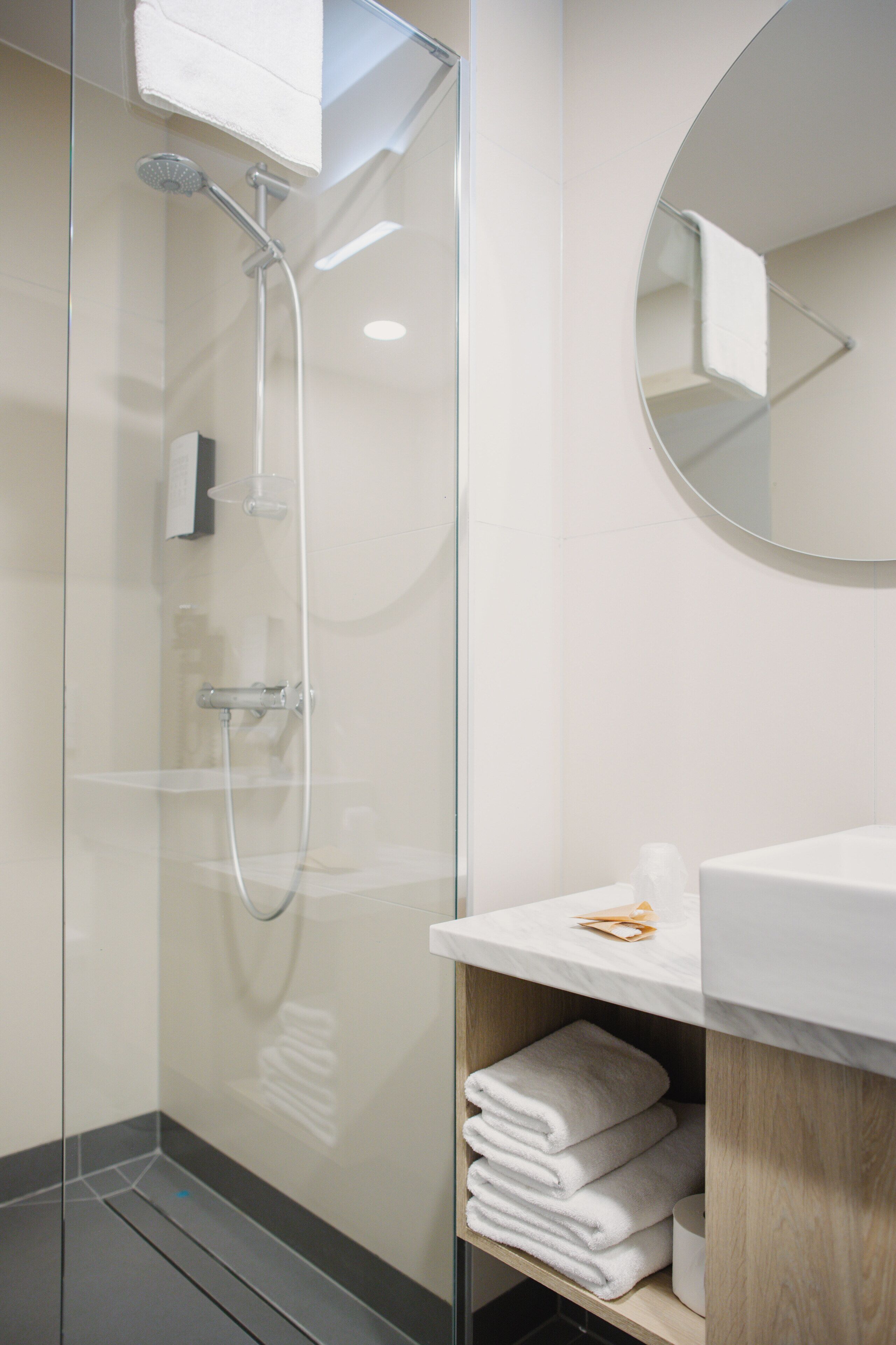 Een moderne badkamer met een douchecabine van glas, een witte wastafel en een ronde spiegel.