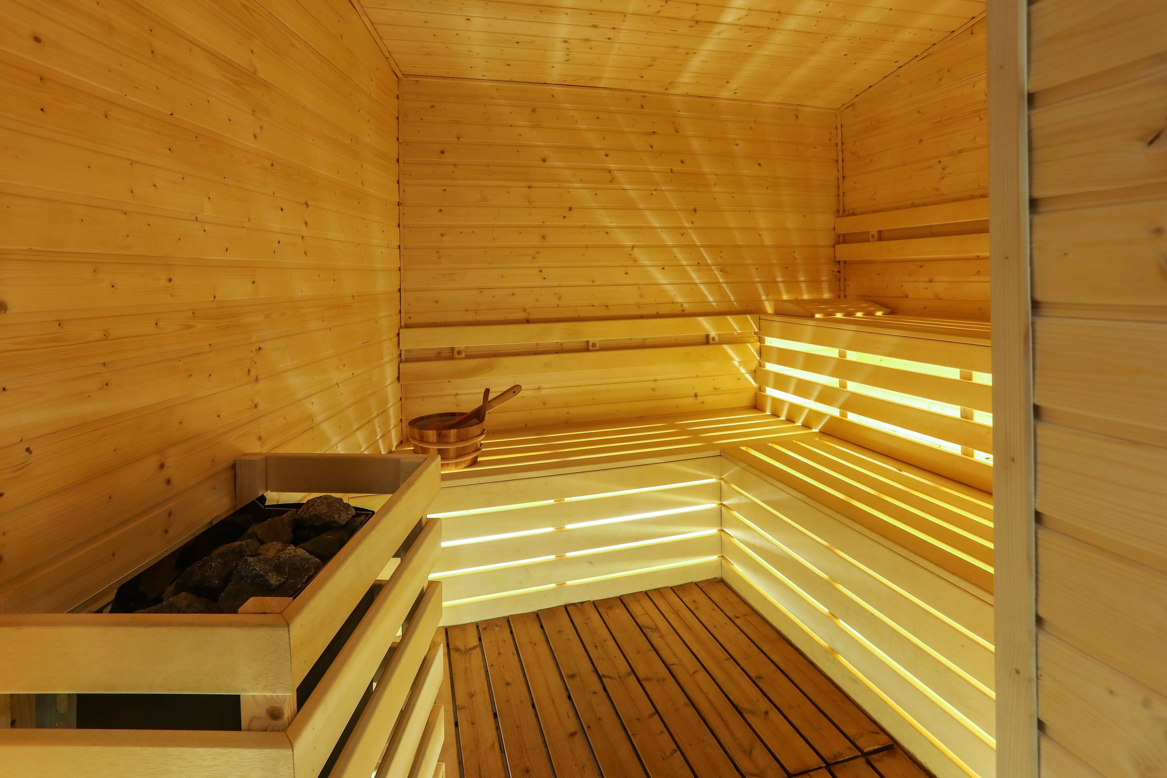 A sauna with wooden walls and benches, a wooden floor, and a heat source in the corner.