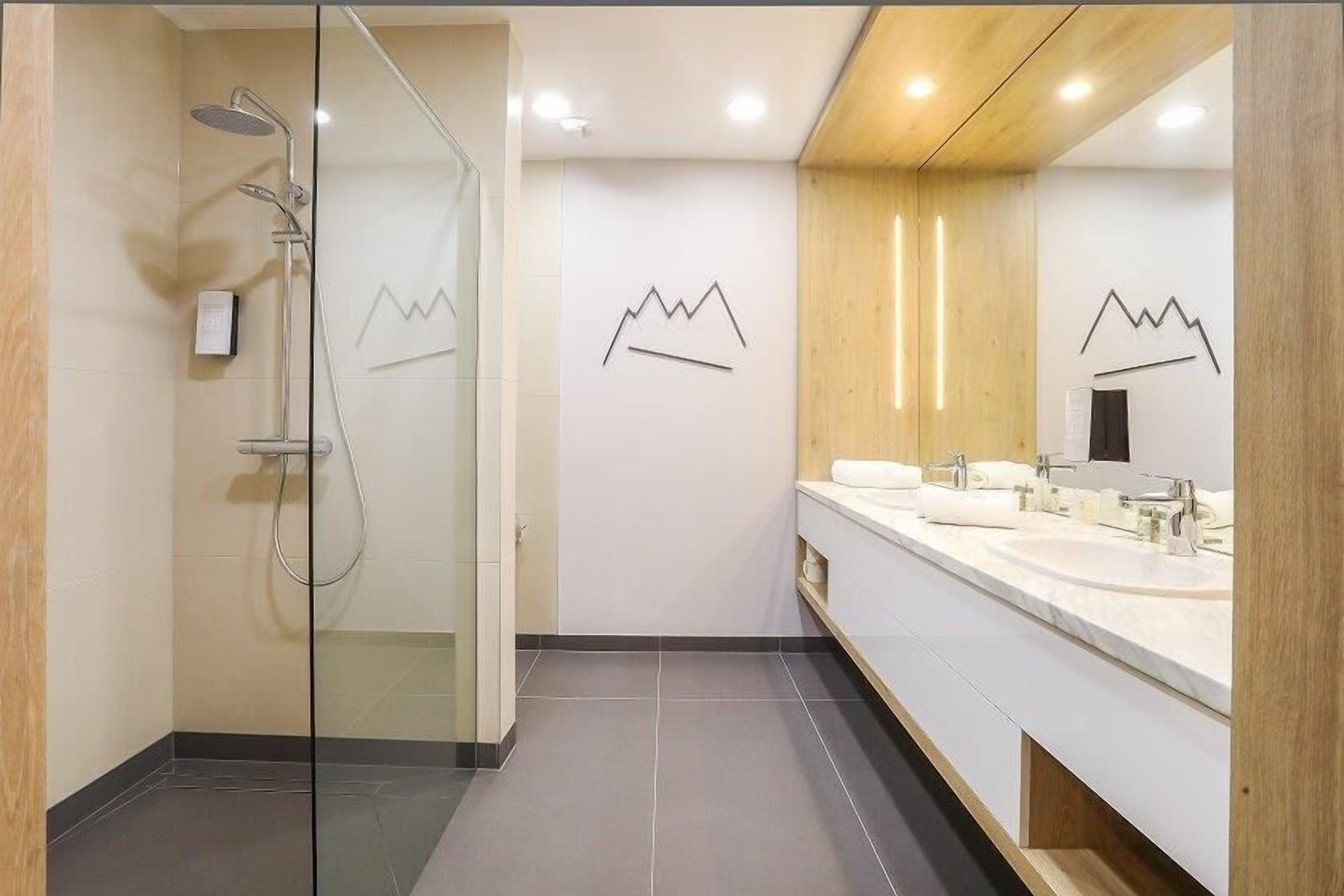 Un bagno moderno con doccia vetrata, un ampio specchio e due lavandini.