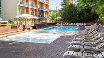 A pool area with lounge chairs and a building with balconies.