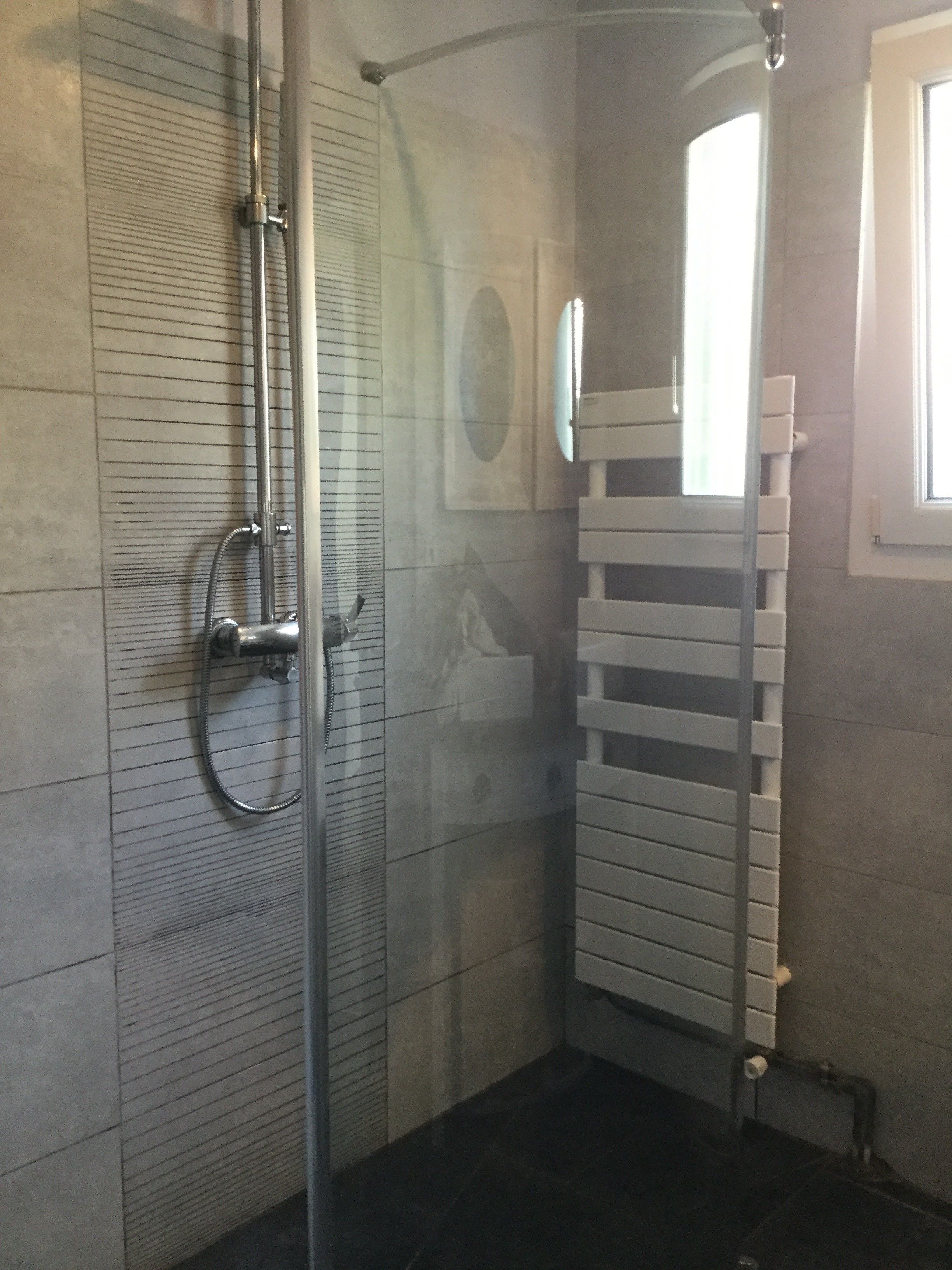 A bathroom with a glass shower enclosure, a towel rack, and a window providing natural light.
