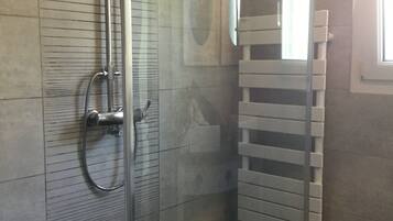 A bathroom with a glass shower enclosure, a towel rack, and a window providing natural light.