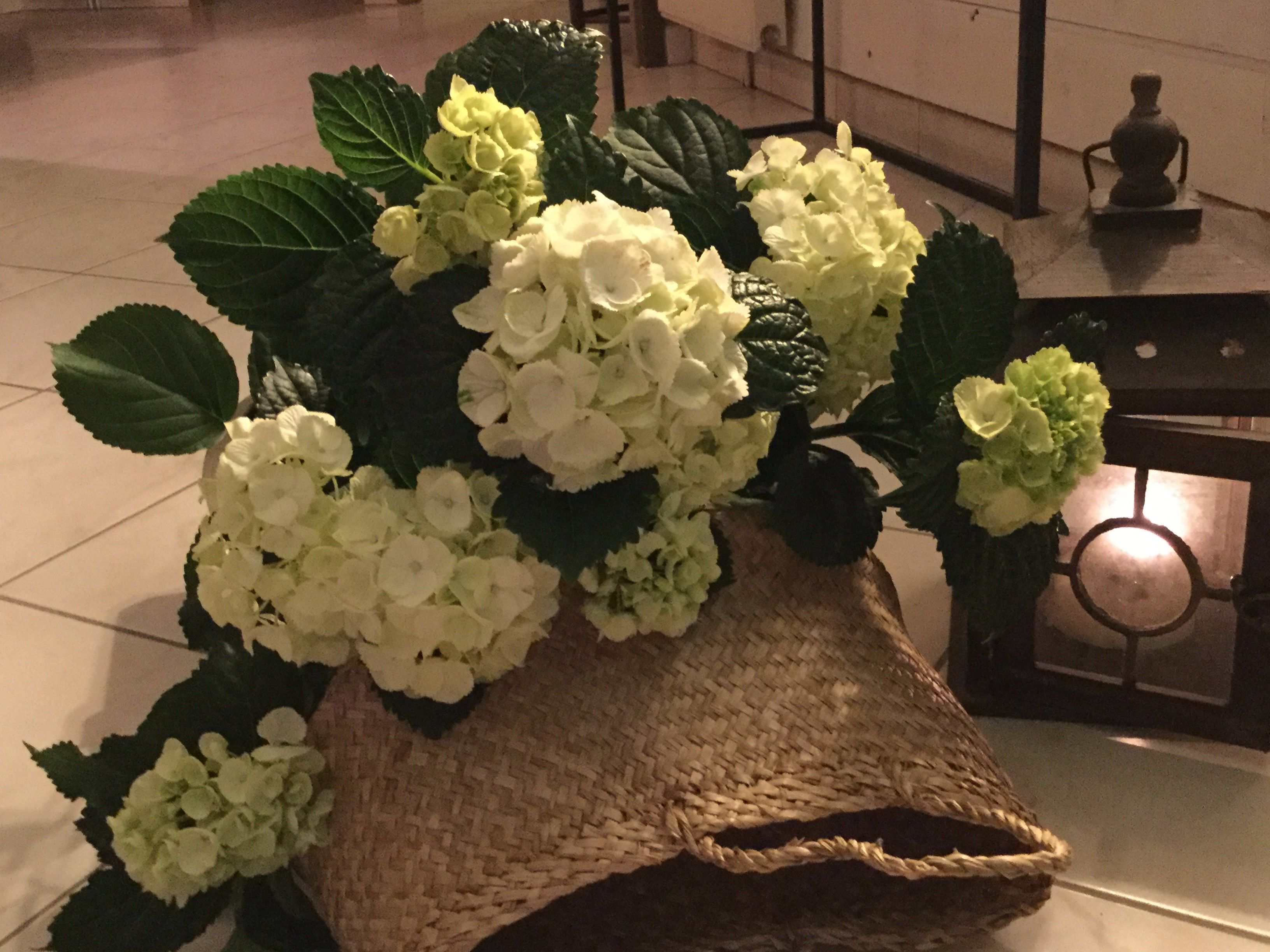 Cesto de vime cheio de flores brancas e verdes sobre um chão de azulejos.