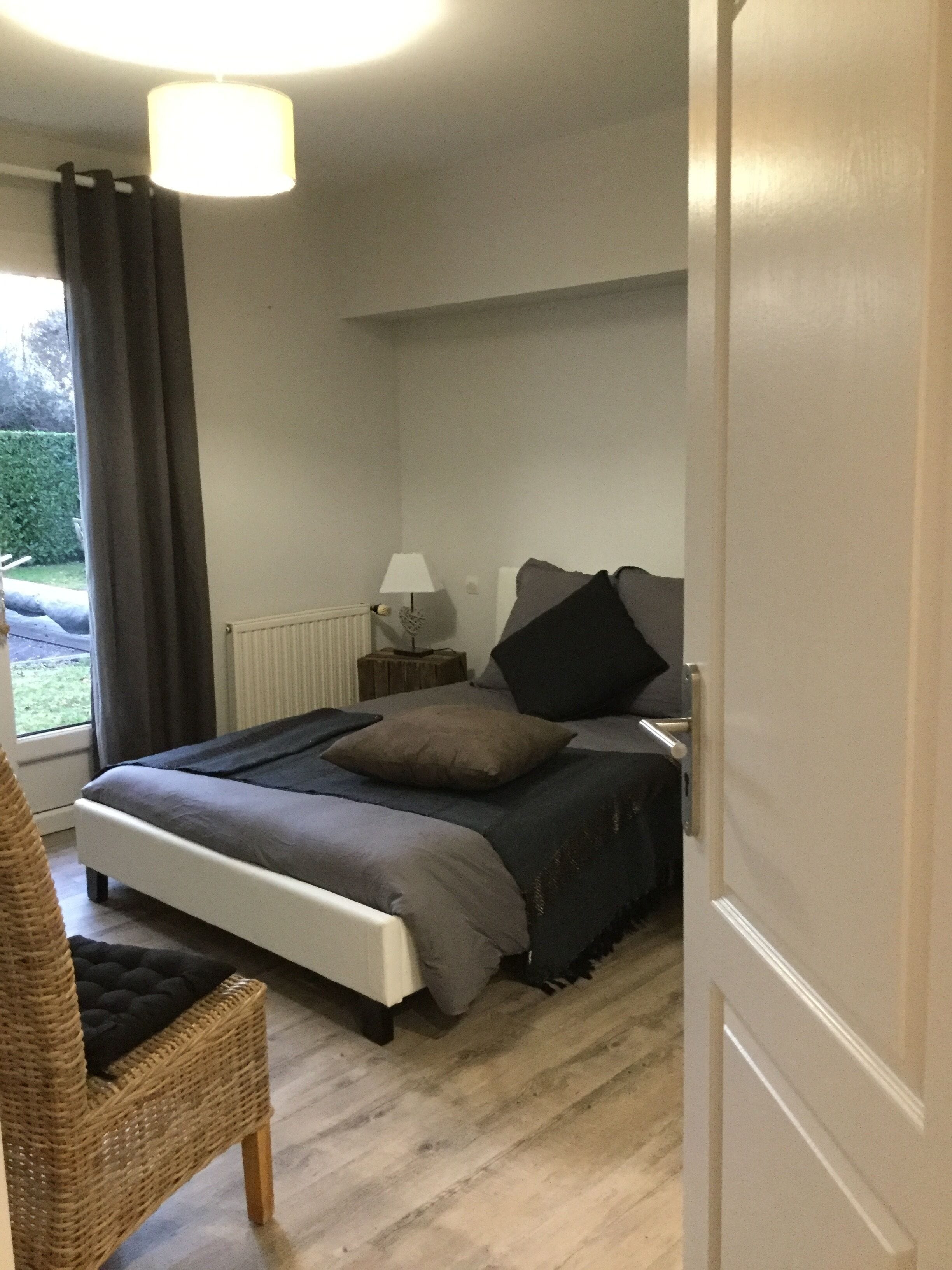 A bedroom with a bed, a nightstand, a lamp, a chair, and a window with curtains.