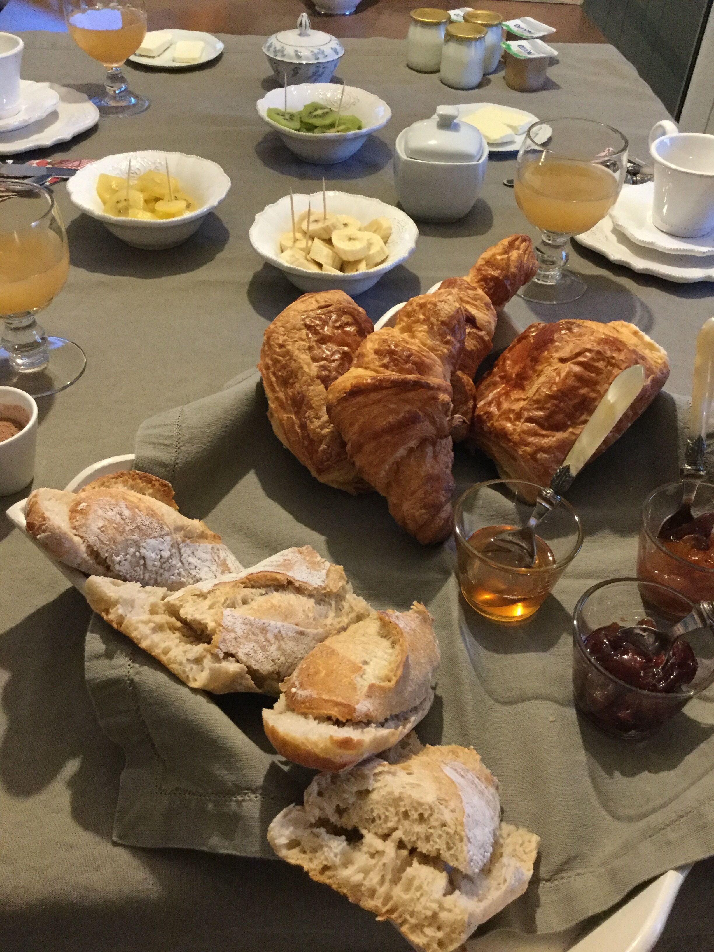 A table set with croissants, bread, fruit, and beverages.