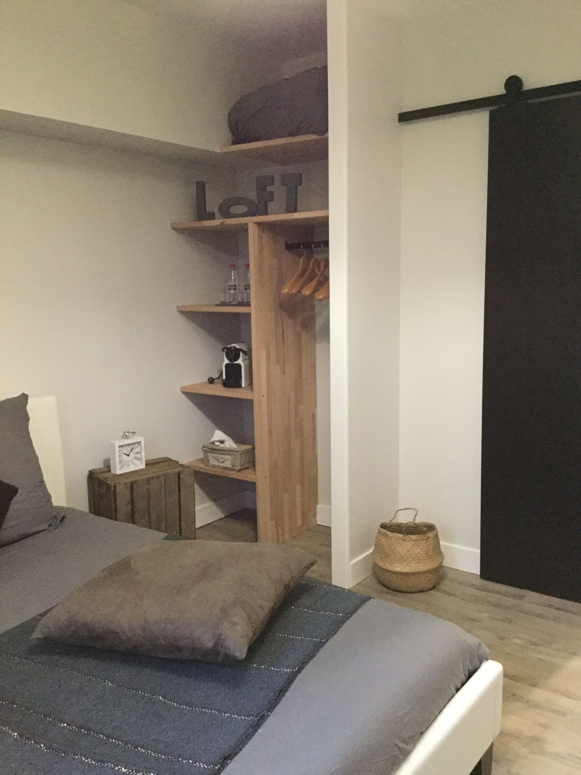 Un dormitorio con una cama, un armario de madera y una mesita con un reloj y una cesta.