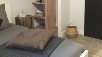 Un dormitorio con una cama, un armario de madera y una mesita con un reloj y una cesta.