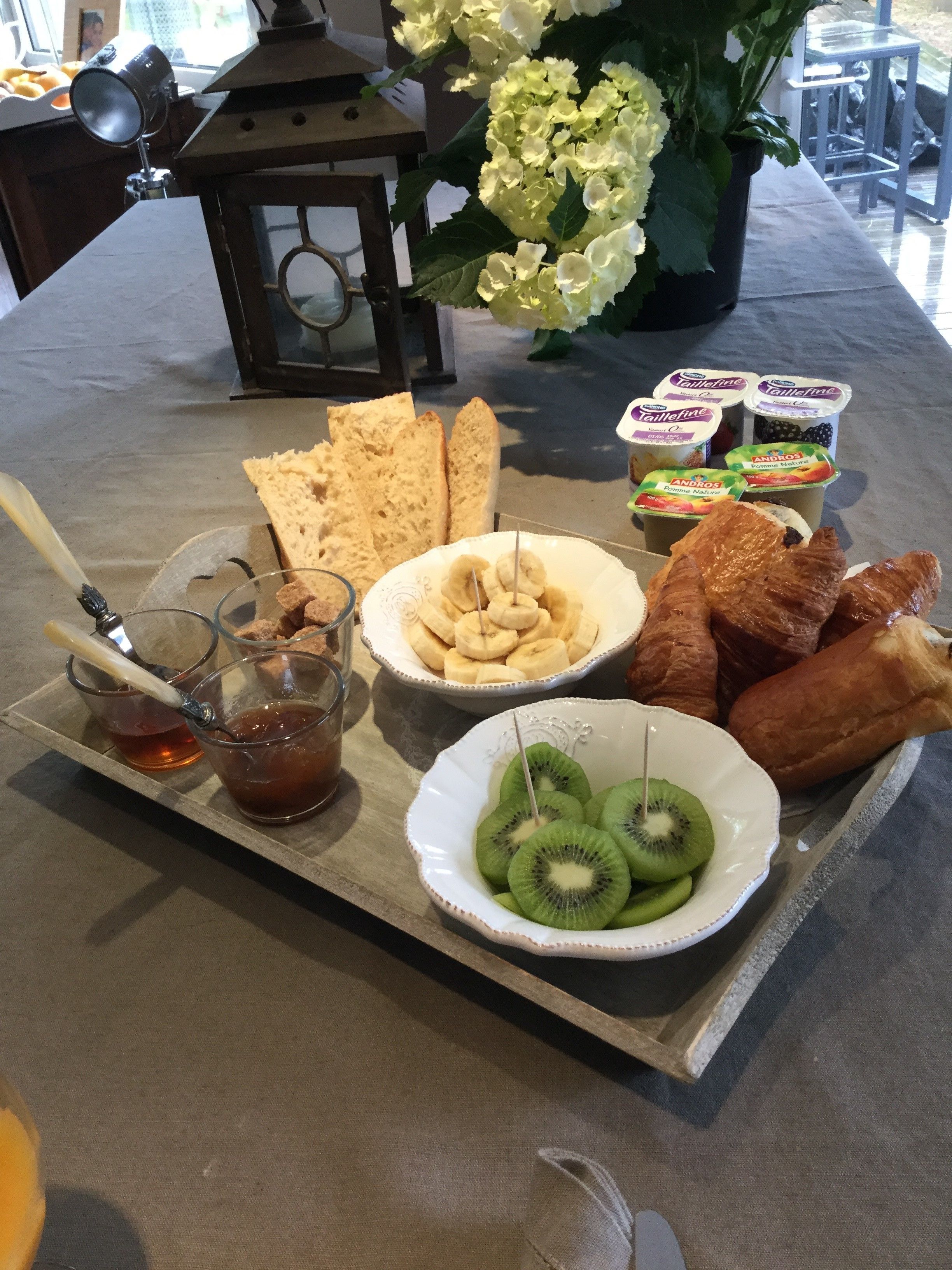 A table with a variety of food items including bread, bananas, kiwi, and yogurt.