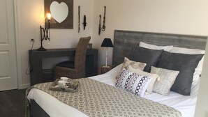 A neatly made bed with patterned bedding, a side table with a tray of items, a chair, and a wall-mounted mirror. - La Maison des Eaux Claires (Puymoyen)