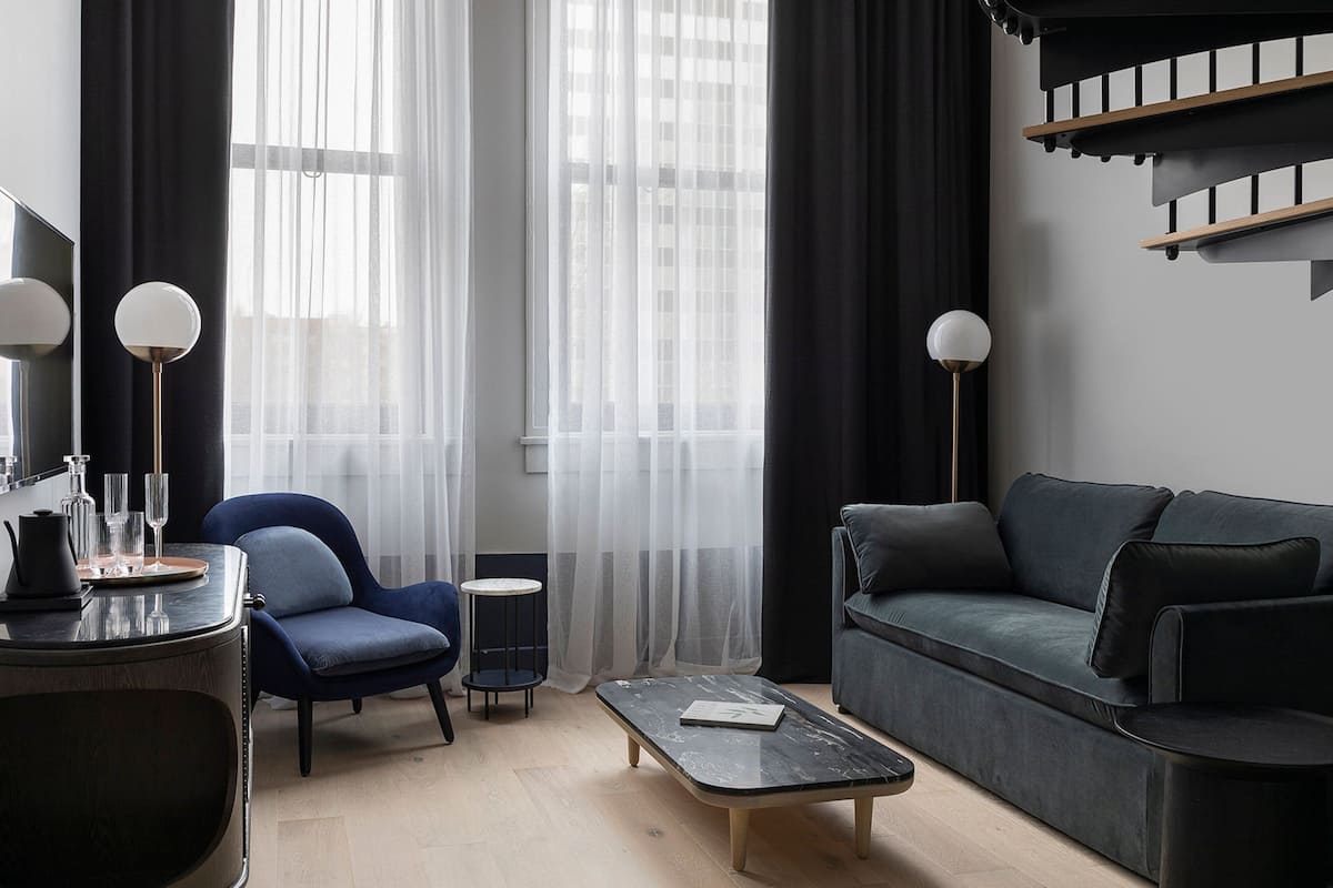 A modern living room with a dark blue sofa, a round coffee table, a blue armchair, and a small side table.