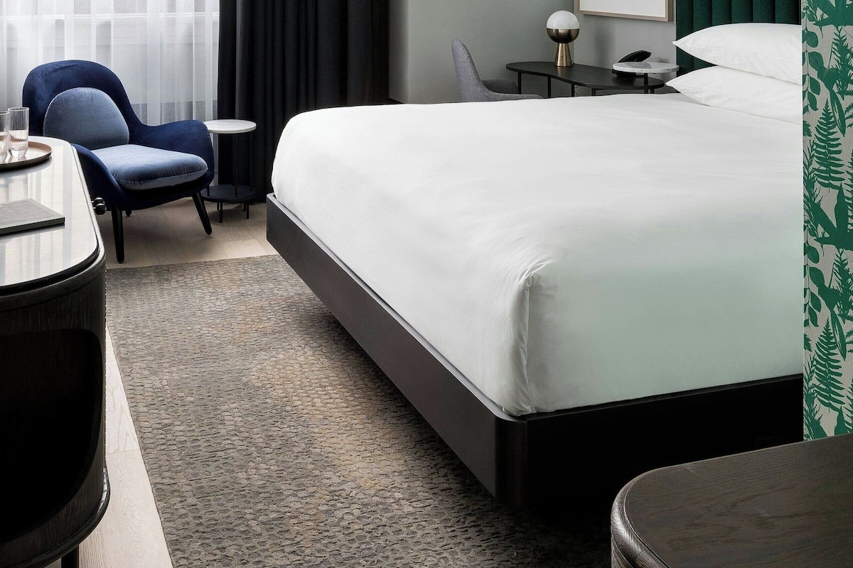 A modern hotel room with a large bed, a desk with a chair, a small table, and a picture on the wall.