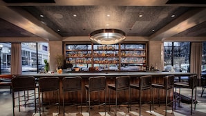 A bar area with a long counter, multiple stools, and a well-stocked shelf of bottles. - Woodlark Hotel Portland, a Tribute Portfolio Hotel (Portland)