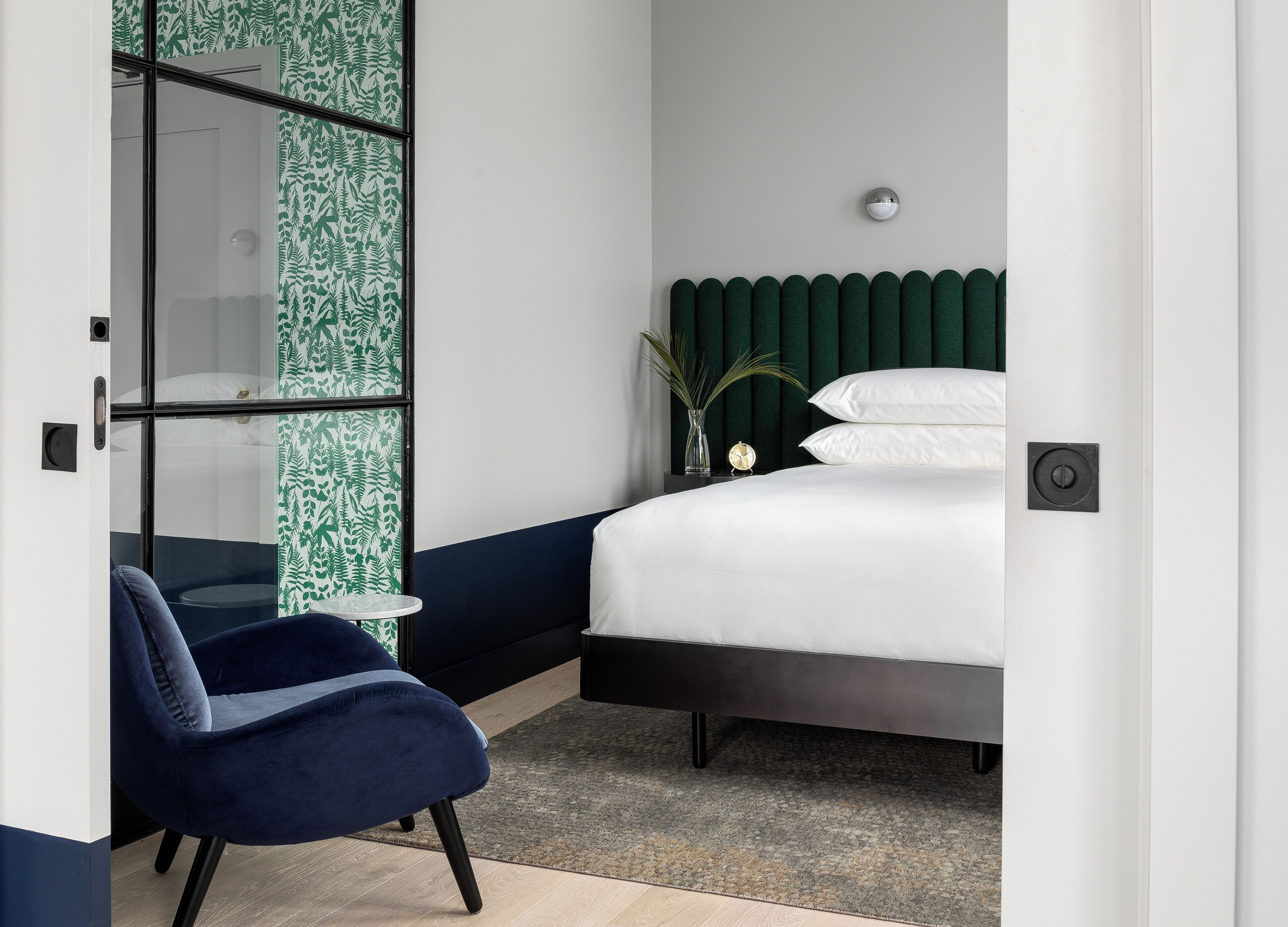 Quarto com cama, cadeira, mesa de cabeceira, relógio e cabeceira verde.