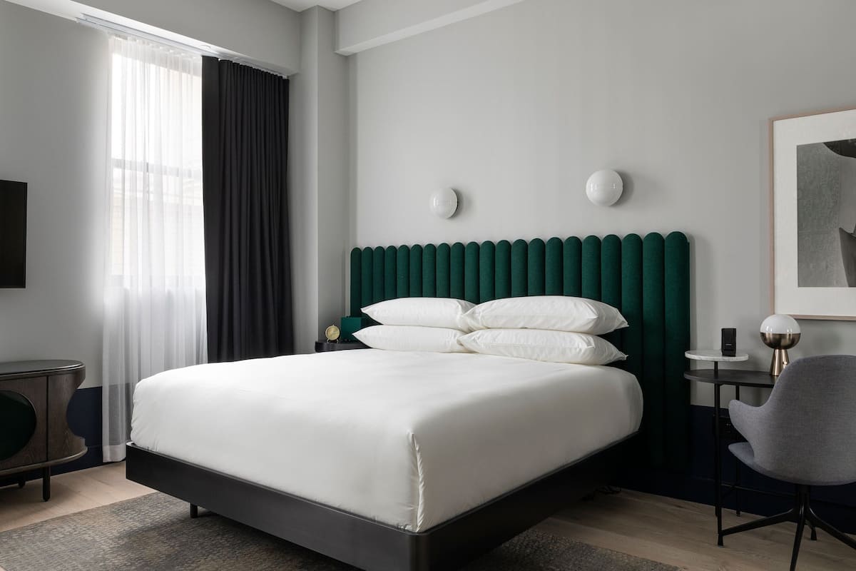 A modern hotel room with a large bed, a desk, a chair, and a view of the city.