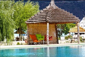 A poolside area with a thatched gazebo, lounge chairs, and a mountain backdrop. - Le Vallon Vert - Club Équestre (Tigrigra)