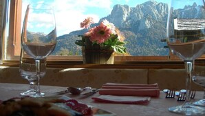 Une table avec deux verres à vin, une assiette de nourriture et une fenêtre donnant sur une vue sur les montagnes.