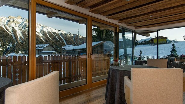 Un balcon spacieux doté d’un plafond en bois, de grandes portes-fenêtres coulissantes et offrant une vue sur une montagne enneigée et un lac.