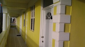 A corridor with a yellow wall, a white door with a window, and a small balcony visible in the background. - Fairwinds Apartments (Portsmouth)