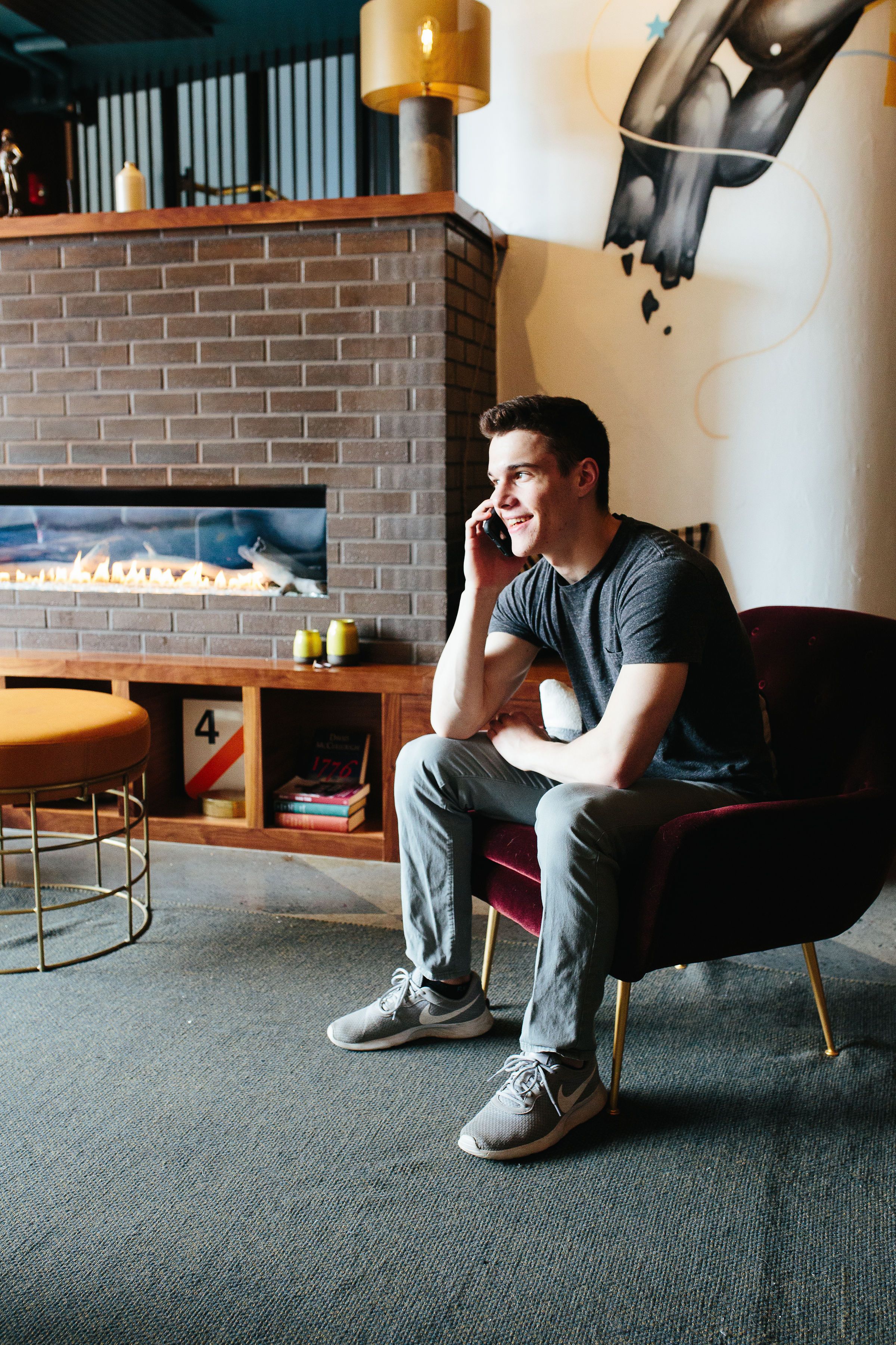 A man sitting on a red chair in a modern room with a brick fireplace, a bookshelf, and a wall mural.