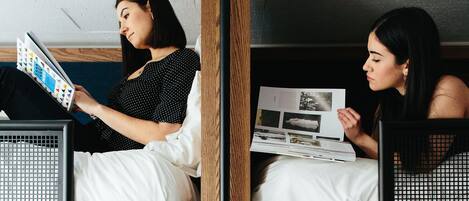 A bunk bed room with two people reading books, a wooden bunk frame, and a blue wall.