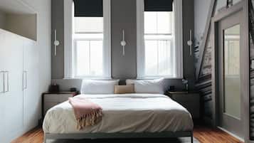 A bedroom with a large bed, two bedside tables, a nightstand, a window with a view, and a door with a view.