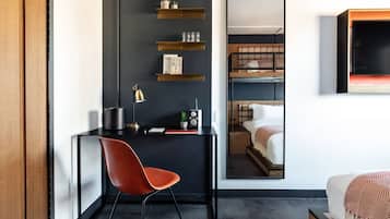 A modern hotel room with a dark wall, a wooden desk, a red chair, a bunk bed, and a mounted TV.