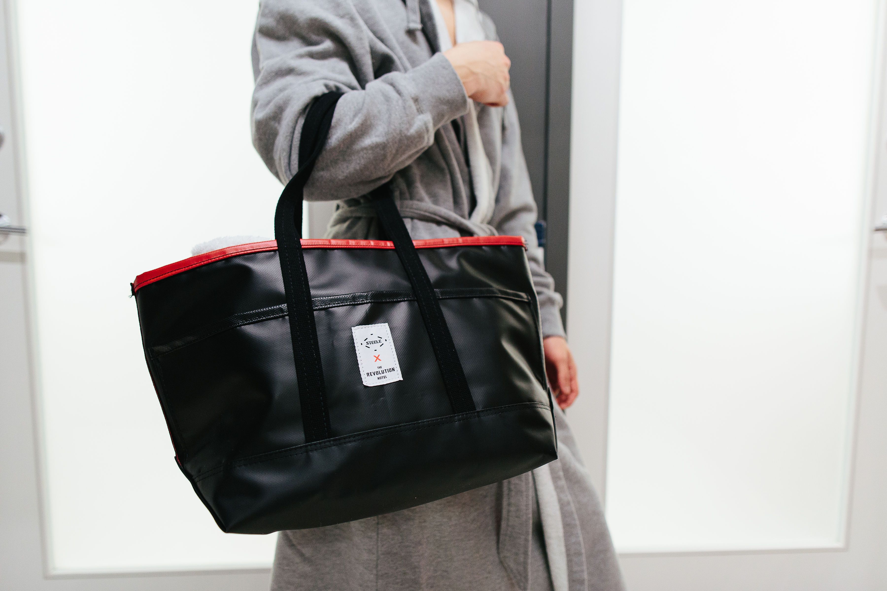 A person carrying a black leather bag with red accents and a white label.