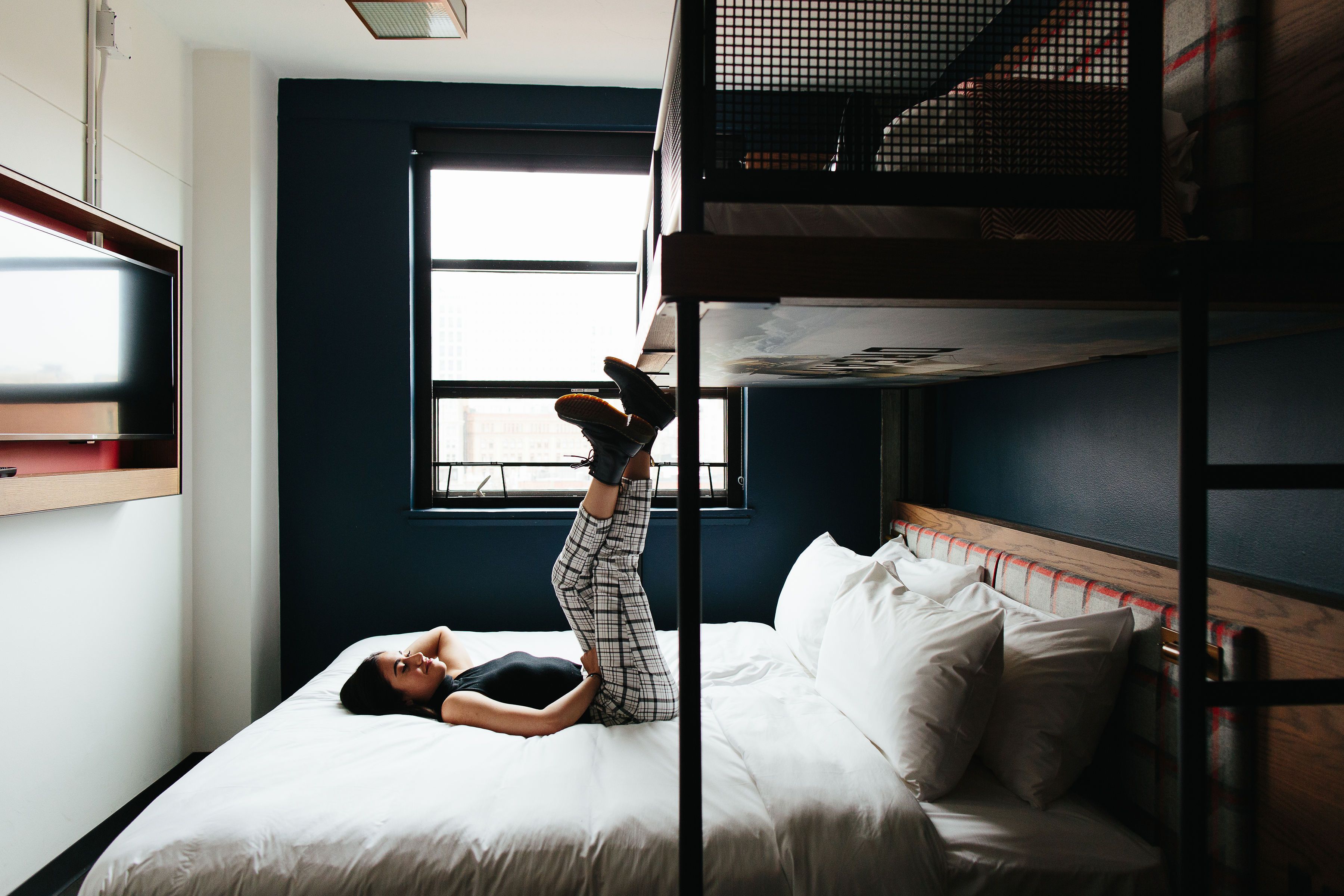 A bunk bed room with a window, a bed, and a person lying on the bed.