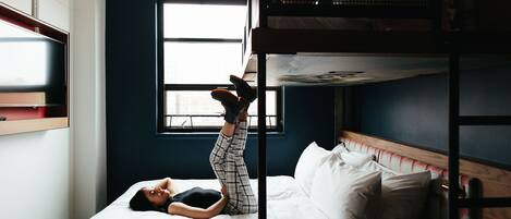 A bunk bed room with a window, a bed, and a person lying on the bed.