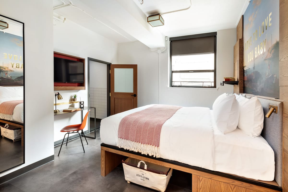 Ein modernes Schlafzimmer mit Bett, Schreibtisch, Stuhl, Fernseher und Fenster.