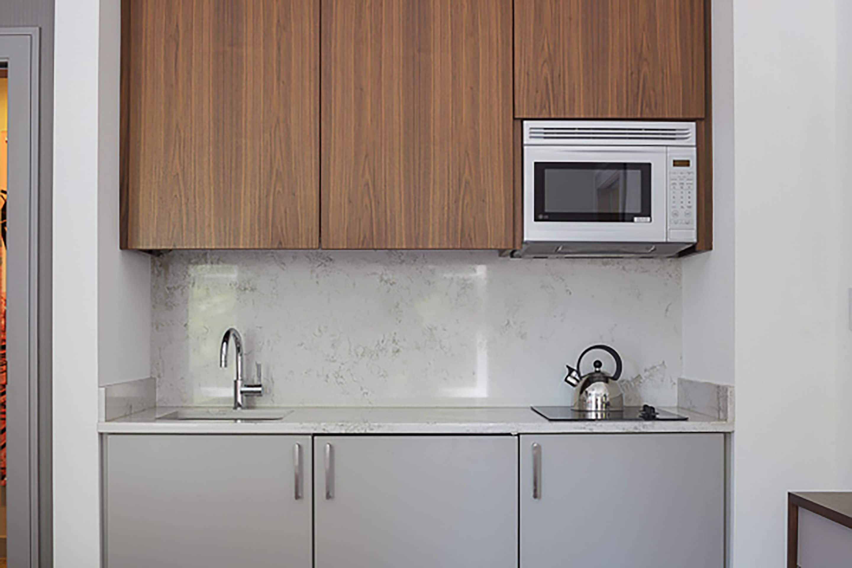 A kitchen with wooden cabinets, a microwave, a sink, and a kettle.