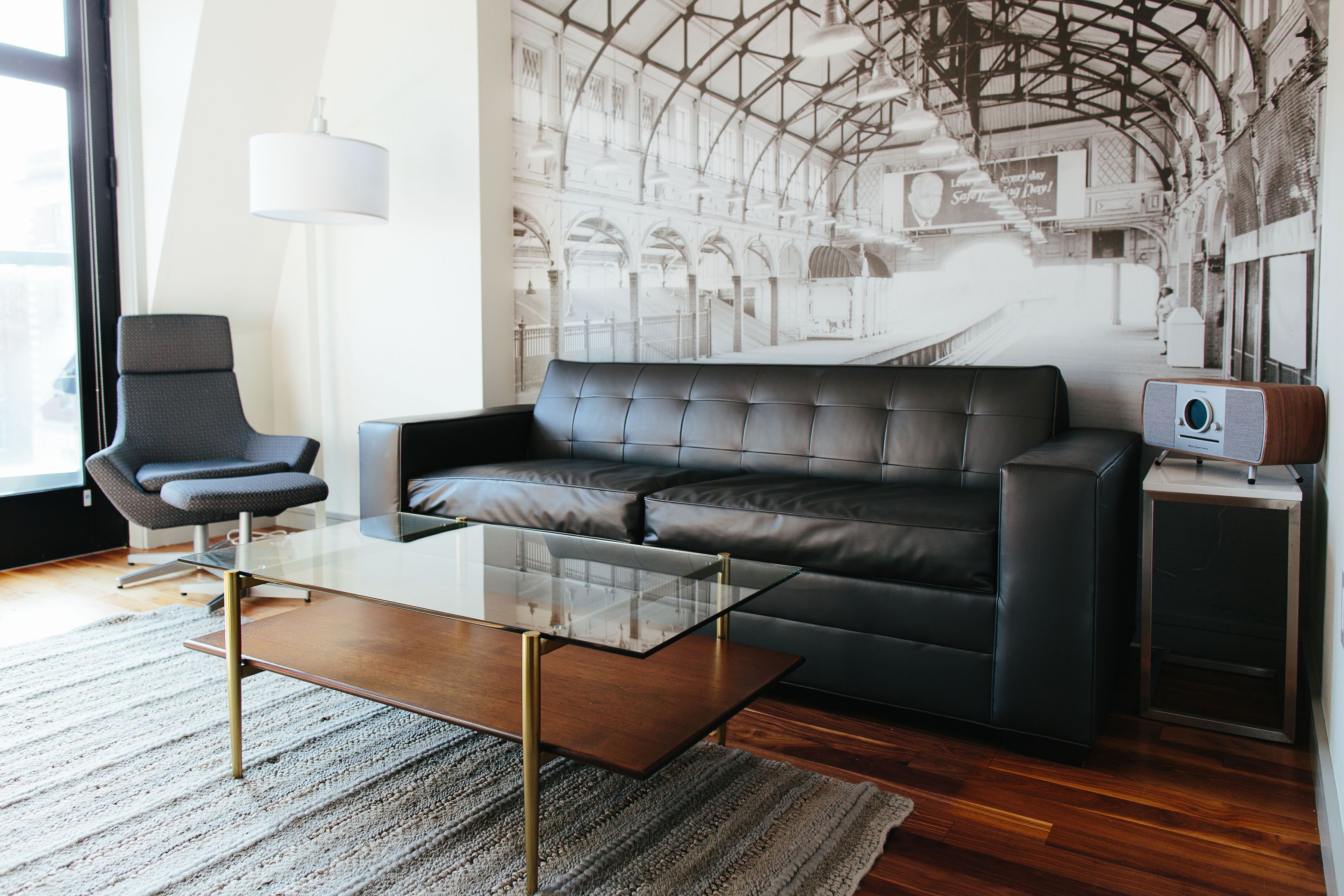 Un salon moderne avec un canapé en cuir, une table basse en verre, un fauteuil et une petite table d’appoint sur laquelle se trouve une radio.