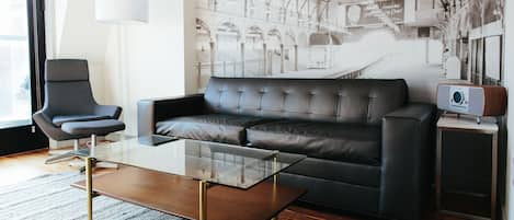 Un salon moderne avec un canapé en cuir, une table basse en verre, un fauteuil et une petite table d’appoint sur laquelle se trouve une radio.