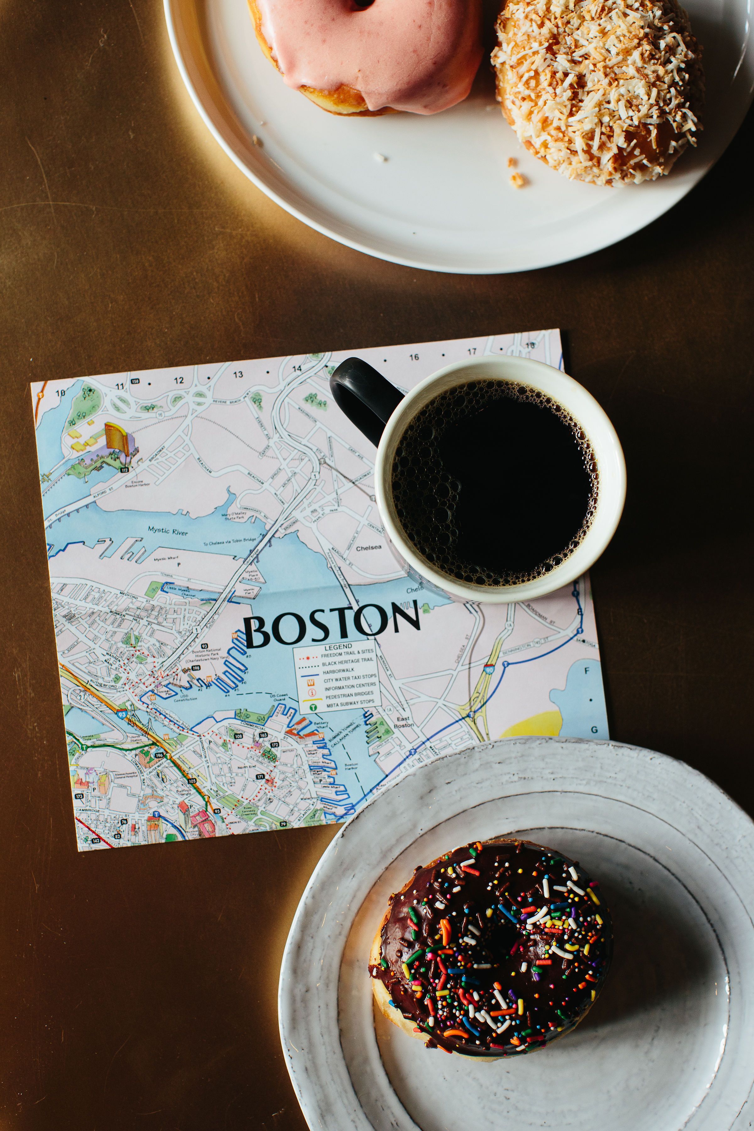 Eine Karte von Boston, ein Teller mit einem Donut, ein Teller mit einem Donut und eine Tasse Kaffee auf einem Tisch.