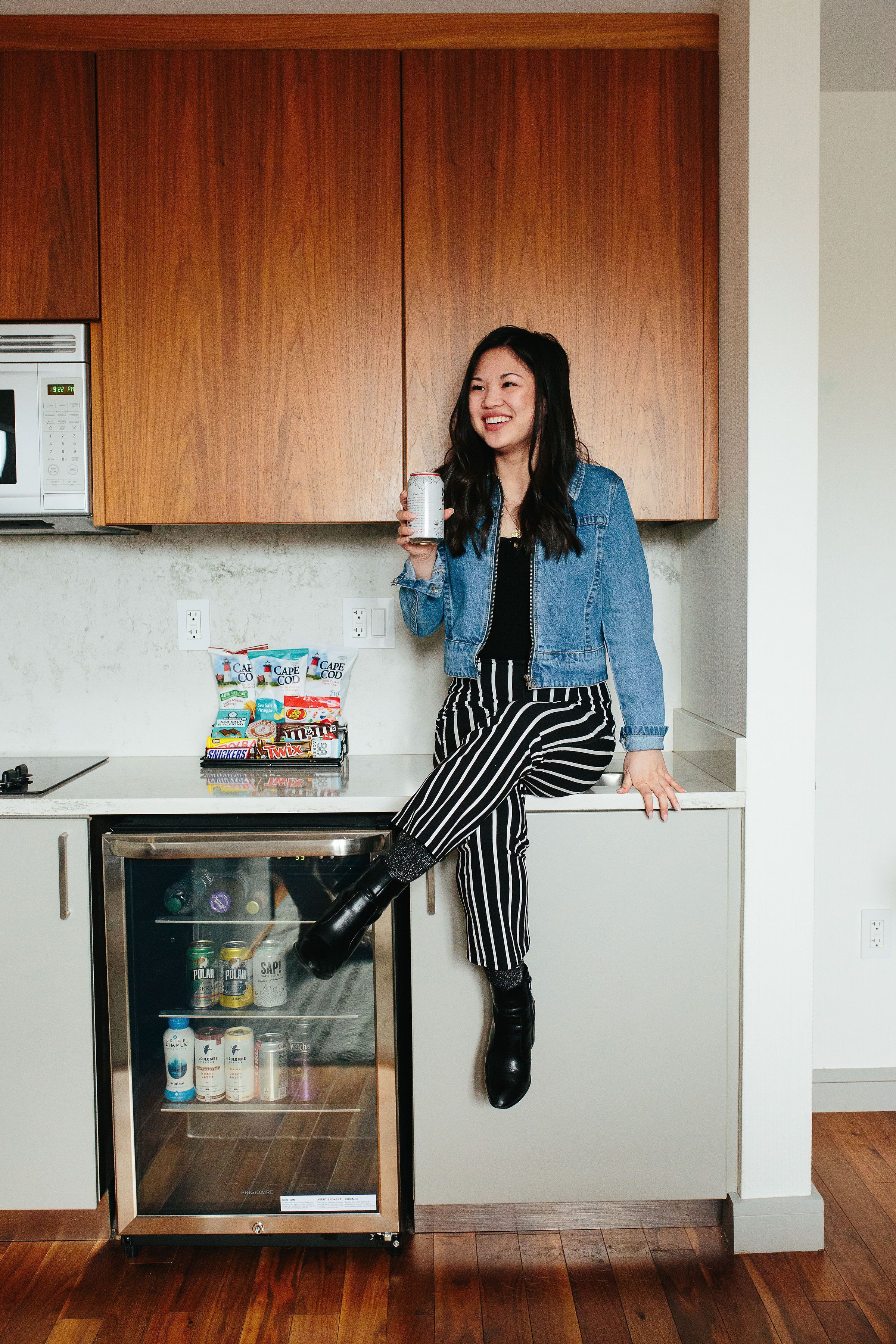 A kitchen with wooden cabinets, a microwave, a refrigerator, and a person holding a can.