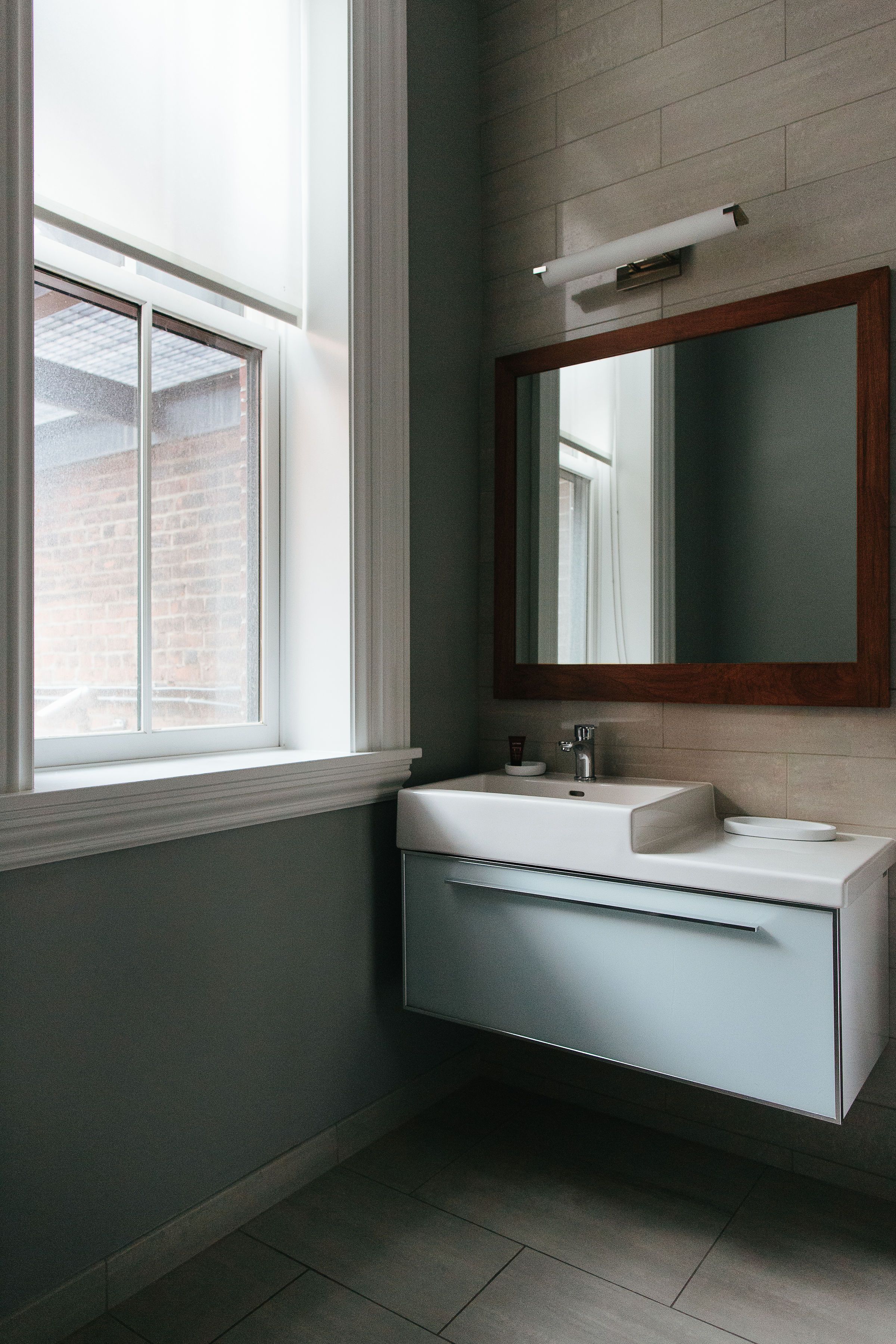 A bathroom with a window, a sink, a mirror, and a light fixture.