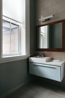 A bathroom with a window, a sink, a mirror, and a light fixture.