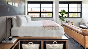 Une chambre d’hôtel moderne dotée d’un grand lit, d’un canapé en cuir et offrant une vue sur la ville grâce à de grandes fenêtres.