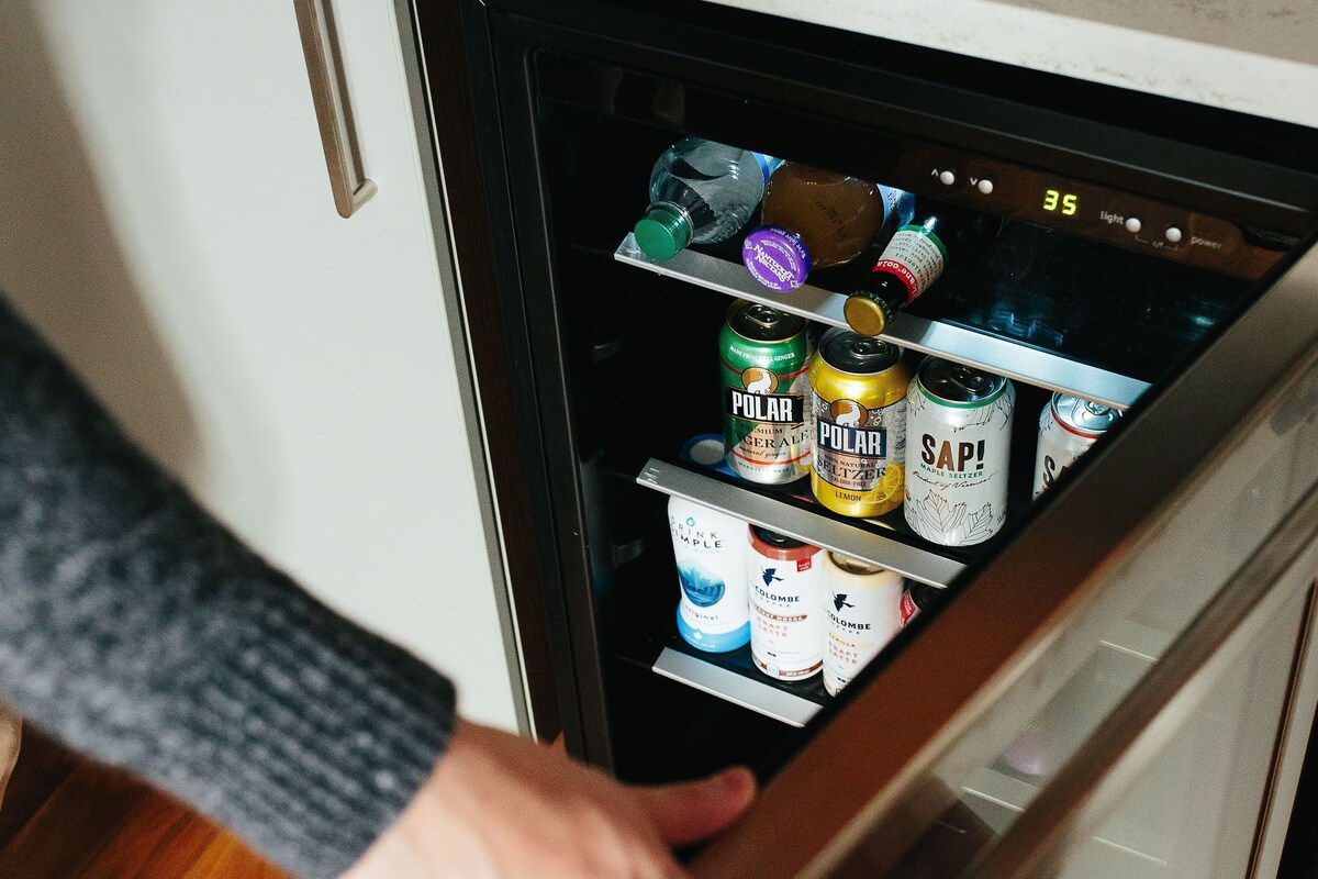 A person opening a refrigerator with various beverages inside.