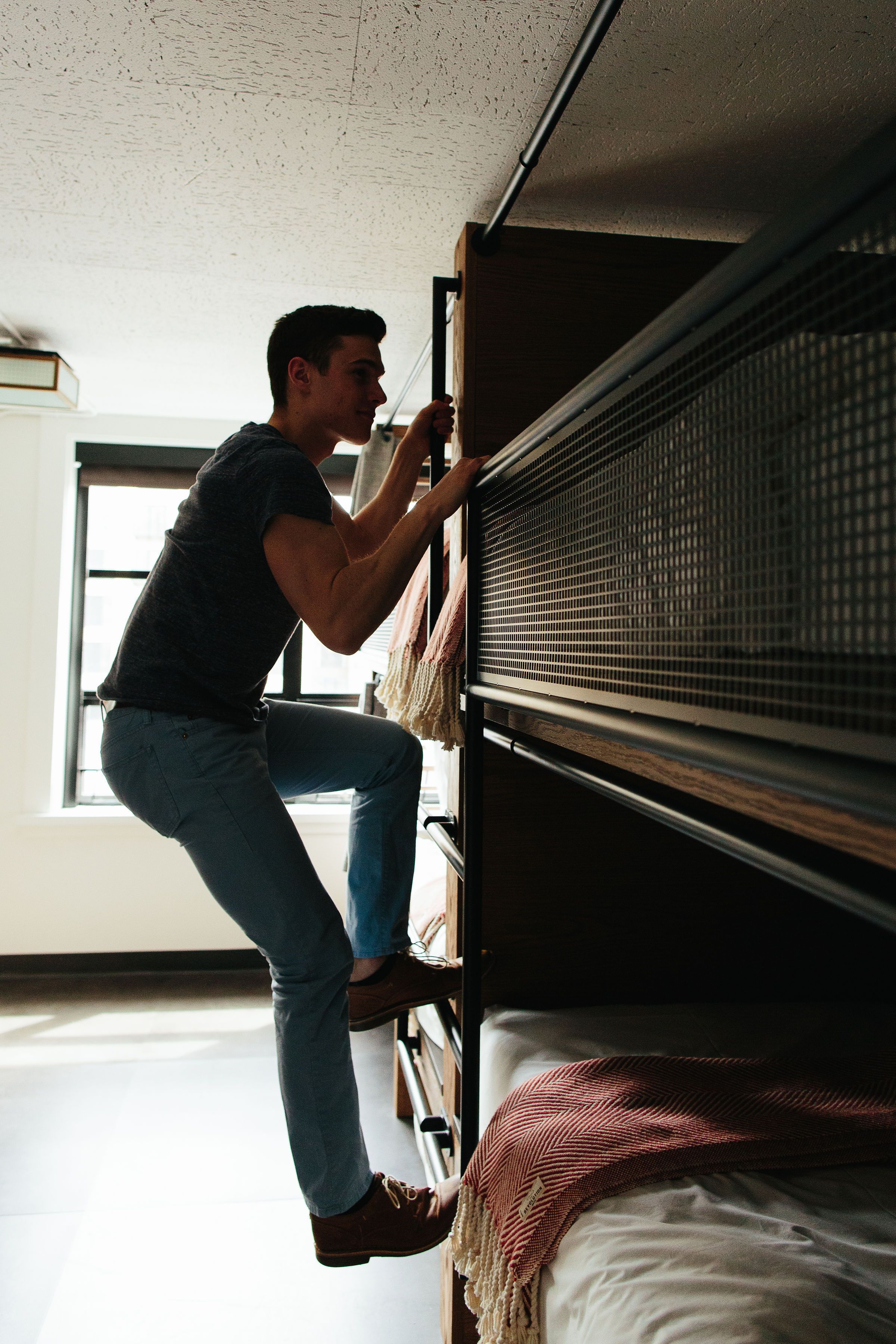A person adjusting a window blind in a room with a bed and a window.